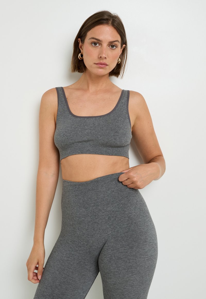 Bralette corta a coste grigia e leggings a vita alta, con una larga fascia elastica e una texture morbida, rifiniti con bordi a contrasto.