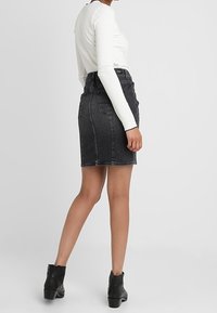 Svart denimkjol med en figursydd form, hög midja, bakfickor och sömnadsdetaljer, parat med en vit långärmad topp och svarta ankelstövlar.