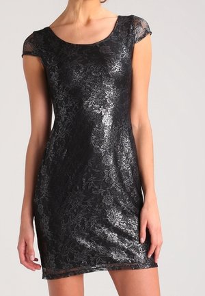 Dopasowana krótka czarna sukienka z kwiatową koronkową nakładką, krótkimi rękawami i okrągłym dekoltem, noszona przez stojącą osobę.