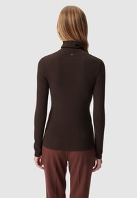 Maglione a collo alto marrone a coste con maniche lunghe, caratterizzato da una vestibilità aderente e un sottile dettaglio di branding sulla parte posteriore. Abbinato a pantaloni marroni.