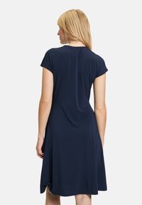 Robe bleu marine à manches courtes en tissu doux et extensible, dotée d'un encolure ronde et d'une jupe évasée avec des fentes sur les côtés pour un mouvement facilité.