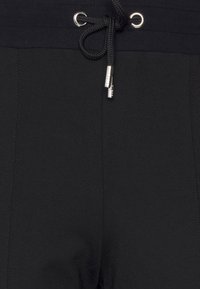 Black athletic shorts with a drawstring waistband, metal eyelets, and contrasting stitching. Made from a smooth, stretchy fabric.