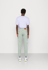 Light purple short-sleeve shirt paired with light green cargo pants featuring pockets and logo embroidery, complemented by gray and white sneakers.
