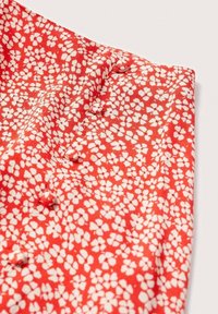 Tissu rouge avec un motif floral blanc. Il présente de petits boutons et une texture lisse, mettant en valeur les détails délicats du dessin.