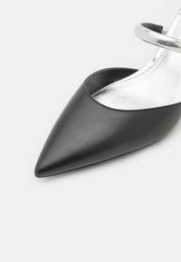 Escarpin en cuir noir avec un bout pointu et une bride de cheville métallique argentée. Texture lisse et design épuré.