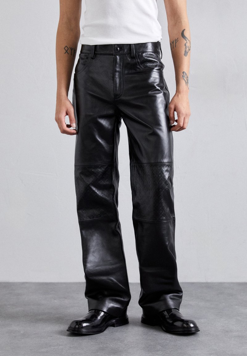 Μαύρο δερμάτινο παντελόνι με άνετη εφαρμογή, που διαθέτει λεία επιφάνεια και υφασμάτινους πίνακες στα κάτω πόδια. Μινιμαλιστικός σχεδιασμός, κλασικό στυλ πέντε τσεπών.