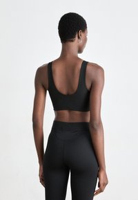 Svart sports-bh med scoop-back design, laget av teksturert stoff. Båret med matchende høytlivet sorte leggings med lommedetaljer.