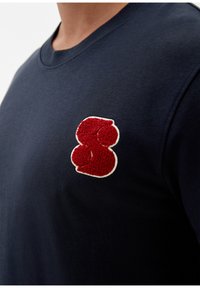 Dunkelblaues Sweatshirt mit Rundhalsausschnitt, ausgestattet mit einem strukturierten roten gestickten Logo auf der linken Brustseite. Weicher Baumwollstoff.