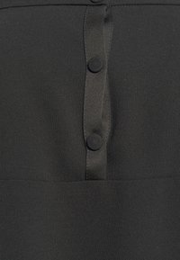 Gros plan sur un tissu noir avec deux boutons recouverts de tissu sur une patte verticale cousue sur le vêtement.