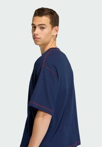 Navy modrý tričko s krátkým rukávem a červenými švy. Design má uvolněný střih a kulatý výstřih. Měkký bavlněný materiál.