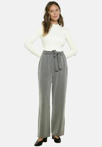 Pilkos dryžuotos plačios kelnės su diržu liemens srityje, derinamos su šviesiai kreminės spalvos ilgomis rankovėmis megztiniu su raukiniais. Juodi bateliai su kulnu užbaigia aprangą.