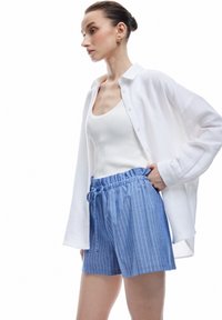 Vit långärmad skjorta med knappar, lätt tyg; figurnära vit linne; blå randiga shorts med elastiskt midjeband och dragsnodd.