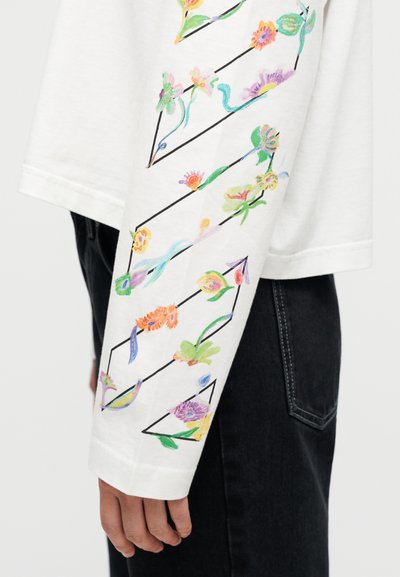 Λευκό μακρυμάνικο πουκάμισο με πολύχρωμη κεντητή ανθοδέσμη κατά μήκος του μανικιού, με μαύρα γεωμετρικά περιγράμματα και άνετη εφαρμογή.