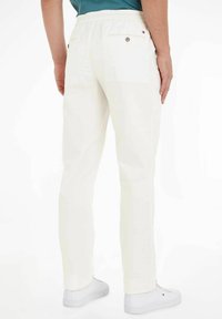 Weiße Baumwollhosen mit einem elastischen Bund, einer Gesäßtasche und einer glatten Textur, kombiniert mit weißen Turnschuhen.