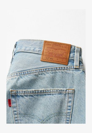 Lichtblauwe denim jeans met een tan leren patch op de tailleband, voorzien van stikdetails en een rode label op de achterzak.
