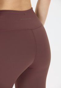 Burgundy höga leggings i en mjuk, stretchig tyg, med subtila sömdetaljer och "ENDURANCE"-logotypen längs midjebandet.