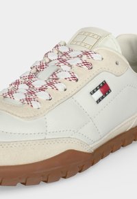 Бели маратонки Tommy Jeans с червено-бели шарени връзки и кафява гумена подметка, с логото на Tommy Jeans отстрани и на етикета.
