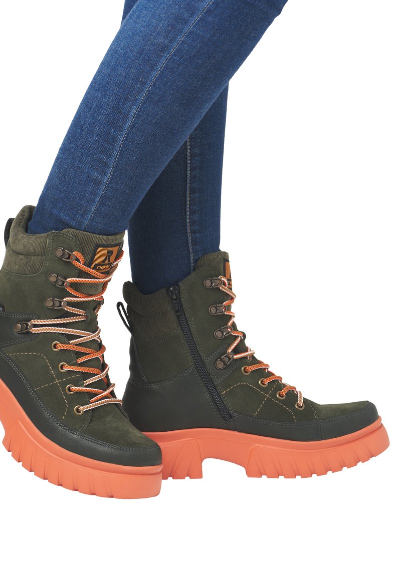 Bottes montantes en daim vert foncé et cuir noir avec des lacets et des accents orange. Semelle épaisse en caoutchouc orange avec un motif de semelle profond.