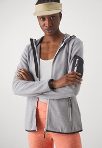 Gray zip-up jacket with a textured finish, black accents, and side pockets. Paired with orange textured leggings. White tank underneath.