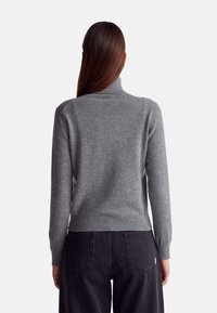 Šedý rolák vyrobený z měkké pleteniny, s vroubkovaným límcem a manžetami. V kombinaci s černými džínami s vysokým pasem.