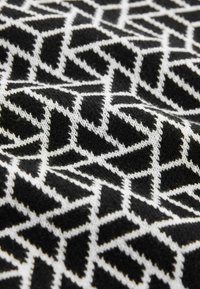 Schwarz-weißer, gemusterter Stoff mit einem winkligen geometrischen Design und einer strukturierten Strickoberfläche. Der Kontrast zwischen den Farben ist stark.
