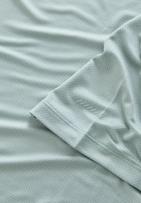 Hellblaues Sporthemd aus strukturiertem Stoff mit einem dezenten hexagonalen Muster, kurzen Ärmeln und einem genähten Saum.