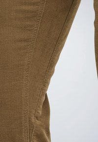 Pantalones de tela marrón con una textura suave, que presentan un sutil patrón de ribetes verticales y costuras contrastantes a lo largo de las costuras laterales.