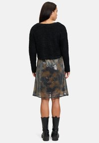 Schwarzer, fusseliger, kürzer geschnittener Pullover kombiniert mit einem metallisch gemusterten Rock, der mit Pailletten in braunen und grauen Farbtönen verziert ist, abgerundet mit schwarzen, knielangen Stiefeln.