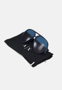 Ochelari de soare cu rame de culoare albastră închisă și lentile nuanțate, așezate pe un toc negru cu un logo alb "A/X" și sistem de închidere cu șnur.