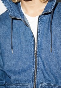 Jeansjacka med dragkedja fram, dragskohuv och två sidofickor. Har en strukturerad yta och kontrasterande svarta dragsnören.