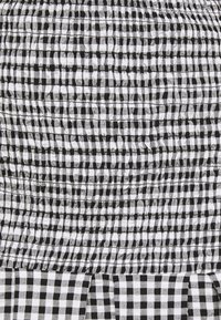 Tissu à carreaux noir et blanc avec une texture smockée ; présente un ourlet à volants ; surface lisse avec des rayures tissées horizontales et verticales.