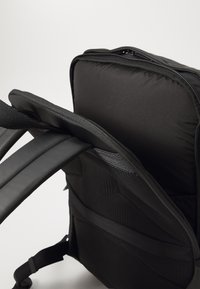 Sac à dos noir avec des bretelles rembourrées, une surface en tissu texturé et un compartiment principal zippé avec un intérieur spacieux.