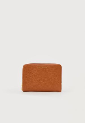 Compact tan leather wallet with gold zipper and "Coccinelle" logo embossed on front, set against a plain white background.
