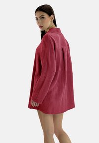Rød, tekstureret skjortekjole med lange ærmer og krave, der har en afslappet pasform og en bagplissé for ekstra stil og bevægelse.