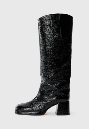 Bota negra hasta la rodilla hecha de charol texturizado con puntera cuadrada y tacón ancho. Acabado suave y brillante con detalles arrugados.