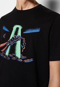 Svart bomull t-shirt med en färgglad grafik av en bil som blir bortförd av en grön stråle, omgiven av blå och rosa moln.