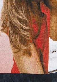 Detailní tkanina s texturovanými vlasy a červeným akcentem na světlém pozadí s černou dolní částí.