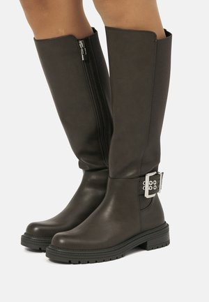 Bottes en cuir marron foncé, hauteur genou, avec une fermeture éclair sur le côté et un détail de boucle. Semelle en caoutchouc durable avec une finition texturée.
