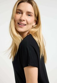 Zwarte korte mouwen top met een relaxte pasvorm, gemaakt van zacht materiaal. Kenmerkt zich door een ronde halslijn en subtiele stiksel details bij de mouwen.