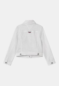 Valkoinen farkkutakki, jossa on klassinen kaulus, pitkät hihat ja nepparit. Tärkeä yksityiskohta on pieni punainen, valkoinen ja sininen koriste takana.