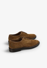 Zapatos oxfords de ante marrón con una textura suave, punta redonda, cinco ojales para los cordones y una suela de goma negra contrastante.