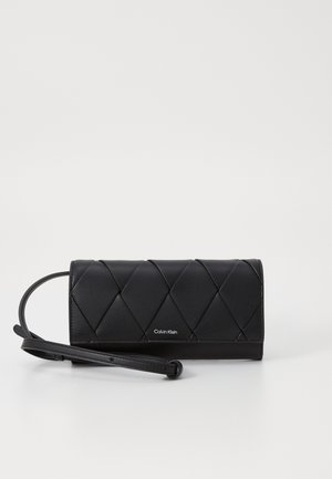 Pochette en cuir matelassé noir avec sangle pour poignet et petit logo Calvin Klein argenté sur le devant.