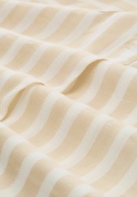 Beige bomuldsstof med hvide bølgete striber, der har en glat tekstur. Designet består af skiftende stripede mønstre.