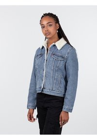Giacca di jeans cropped in azzurro chiaro con colletto in pelliccia sintetica, tasche frontali e chiusura a bottoni. Il tessuto ha una finitura testurizzata classica.