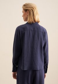 Chemise en lin bleu marine avec col, manches longues et poignets à boutons. Caractérisée par une coupe décontractée et un ourlet légèrement arrondi.