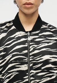 Μαύρο και κρεμ bomber μπουφάν με μοτίβο ρίγες τίγρης, διαθέτει μπροστινό φερμουάρ, ριμπ λαιμόκοψη και διακριτικό λογότυπο στο ύφασμα.