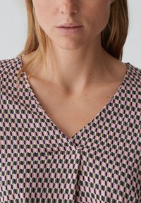Mehrfarbige Bluse mit V-Ausschnitt-Design. Verfügt über ein geometrisches Muster in Rosa, Marineblau und Olivgrün. Glatte Stoffoberfläche, moderate Drapierung.