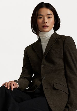 Blazer marrón oscuro hecho de una tela texturizada, con un cuello con muesca, dos botones y un bolsillo en el pecho, superpuesto a un suéter de cuello alto blanco.