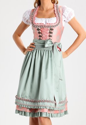 Woman wearing a pink and white dirndl dress with a light green apron tied at the waist and floral trim detailing.