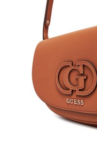 Bolso de hombro de piel marrón con textura de piedra y forma curvada, que cuenta con un prominente logo negro y dorado en la parte frontal y una correa delgada.